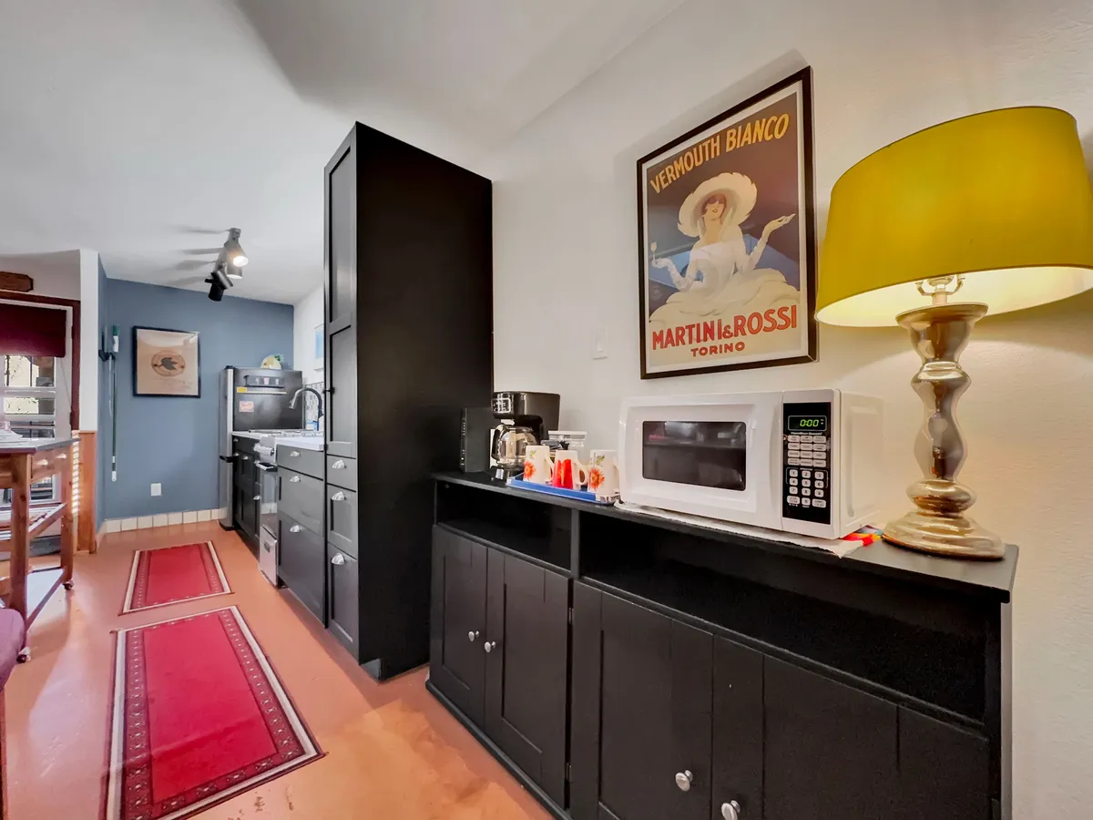 A modern kitchen area featuring sleek black cabinetry, a vintage Martini Rossi poster, a stylish yellow lamp, and vibrant red runner rugs. The room's warm ambiance and clean design provide a sense of comfort and sophistication.