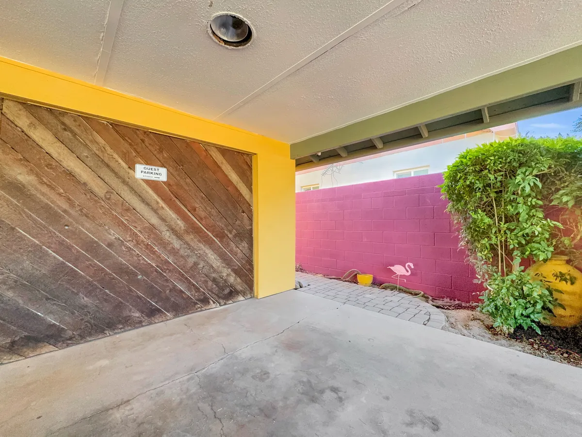 This image shows a carport area with playful color accents on the walls, visible green foliage, and space suitable for shaded parking. The scene projects a welcoming and functional vibe, echoing the convenience and comfort offered by covered parking.