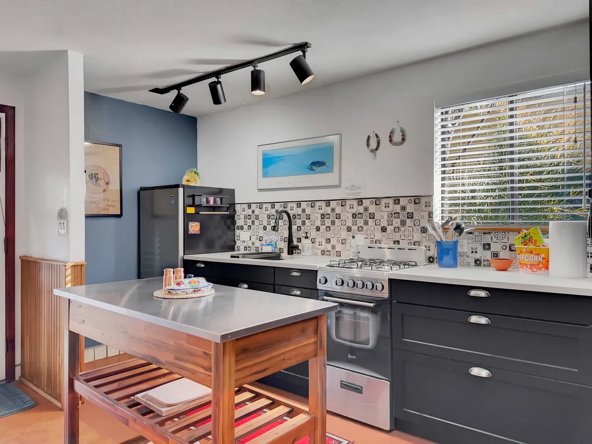 A modern kitchen featuring a central island with a wooden base, stainless steel appliances, a colorful backsplash, and artwork on the wall. The space is well-lit and clearly designed for both cooking and entertaining, showcasing up-to-date kitchen amenities and vibrant decor.