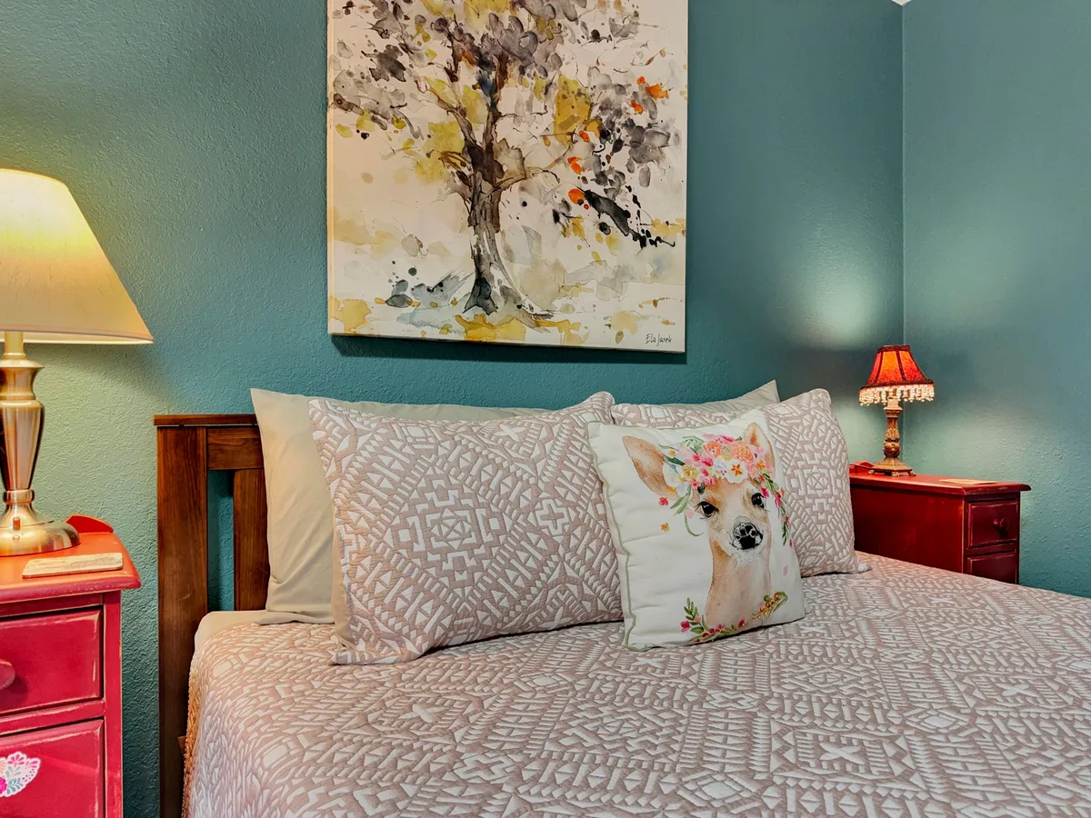 A peaceful sitting area featuring a decorative pillow with a deer, soft table lamp, and tree-artwork. The mood is serene and intimate, suggesting a space designed for quiet moments and personal time.