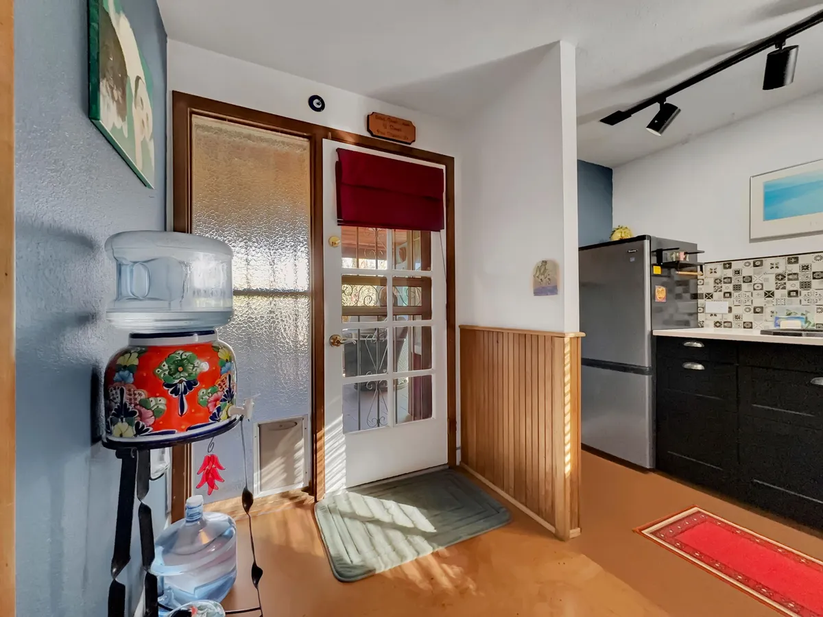 This image features the home's front door with a glass panel, a modern refrigerator, a water cooler, and colorful wall décor. The visible entry point suggests ease of access and hints at the transition between indoor comfort and outdoor adventures.