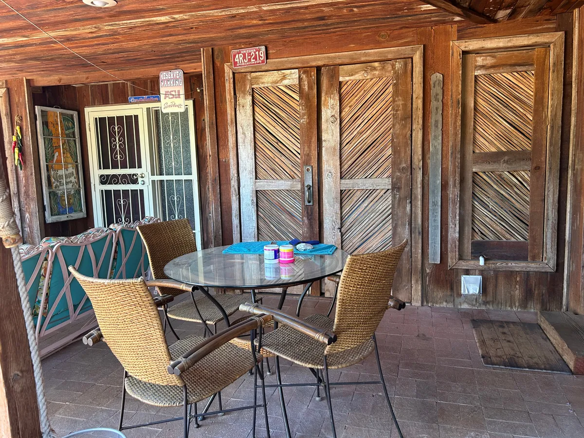 A relaxed dining area with wooden doors, a glass table, woven chairs, and colorful tableware. The setup suggests a welcoming space for casual meals or informal work sessions, with a hint of connection to the outdoors.